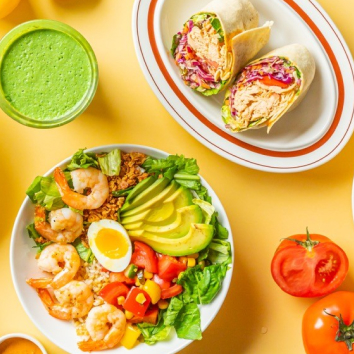 노란 배경에 새우와 아보카도가 담긴 샐러드와 랩이 놓여 있습니다.
